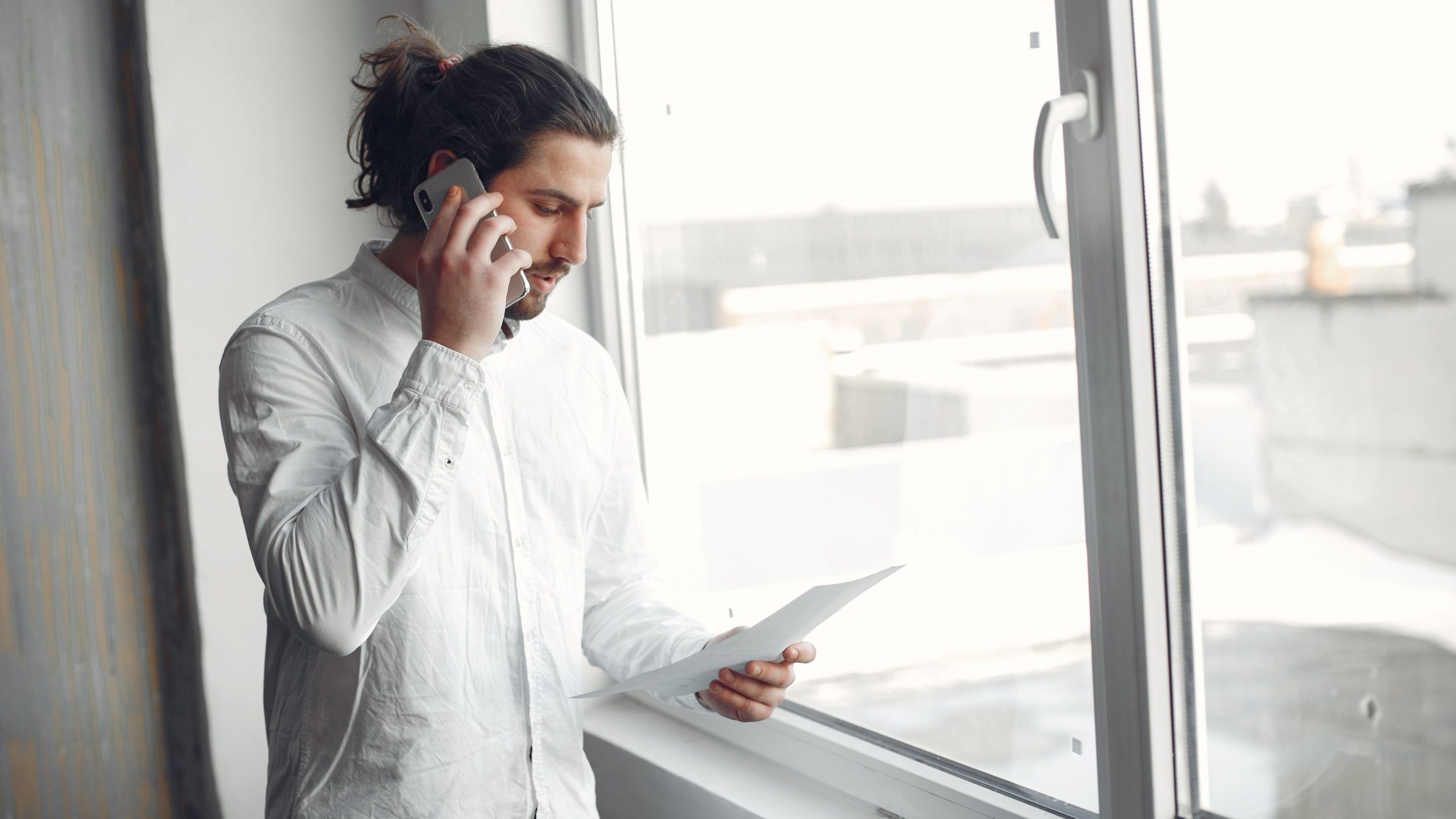 Person talking on a phone while holding a paper in his other hand